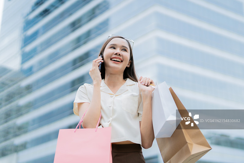 亚洲女人拿着购物袋在购物中心用智能手机交谈图片素材