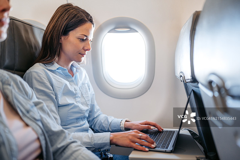 在飞机上用笔记本电脑工作的年轻女人图片素材