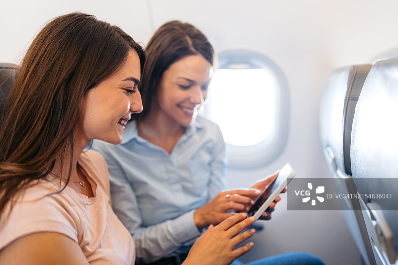 在飞机上使用手机的两位年轻女性朋友图片素材