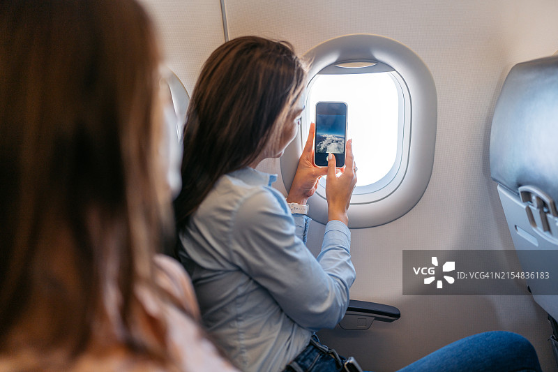 年轻女人在飞机舷窗前拍摄风景图片素材