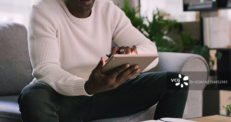 黑人男子在沙发上用平板电脑进行在线研究，了解新闻和信息，作为记者在家工作。图片素材