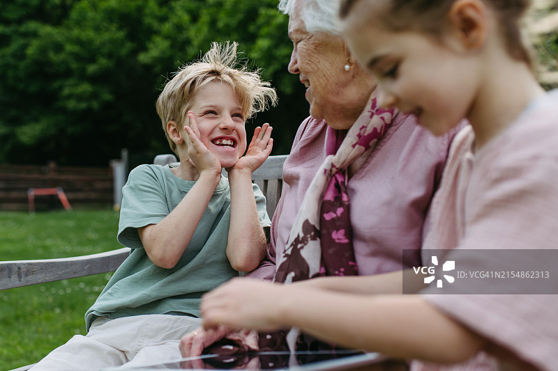 祖母和两个孙辈在花园长椅上做鬼脸图片素材