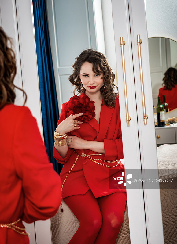 一位穿着红色夹克和红色紧身裤的年轻漂亮女子在镜子前欣赏自己图片素材