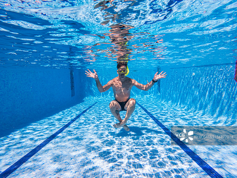 男人戴着护目镜和呼吸管在泳池底部伸展手臂图片素材