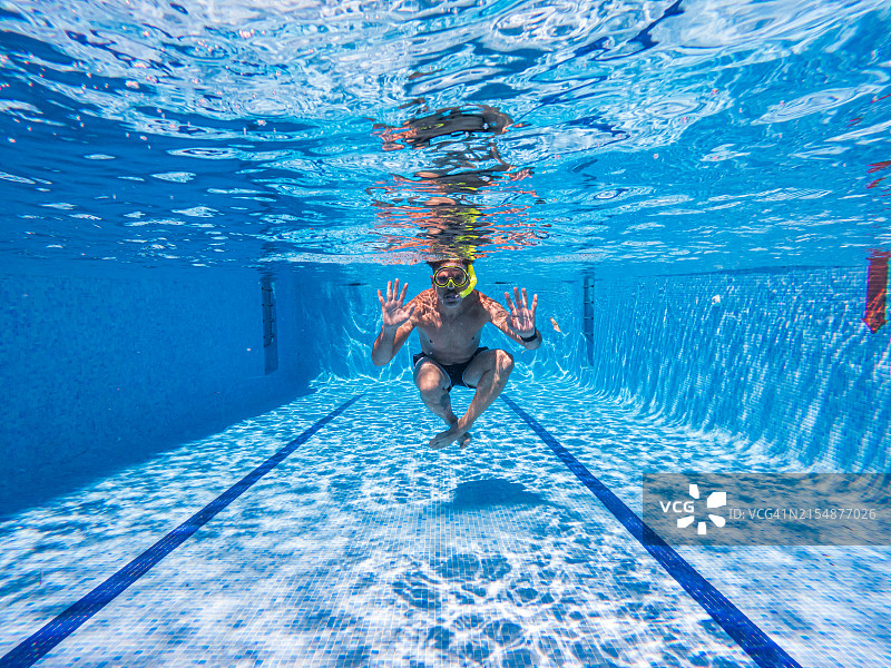 一个男人戴着护目镜和呼吸管在泳池底部游泳，展示他的手掌图片素材