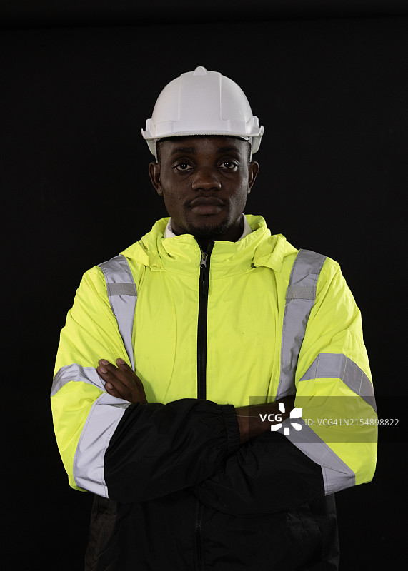 微笑的黑人工程师肖像，戴绿反光安全服和白安全帽。图片素材
