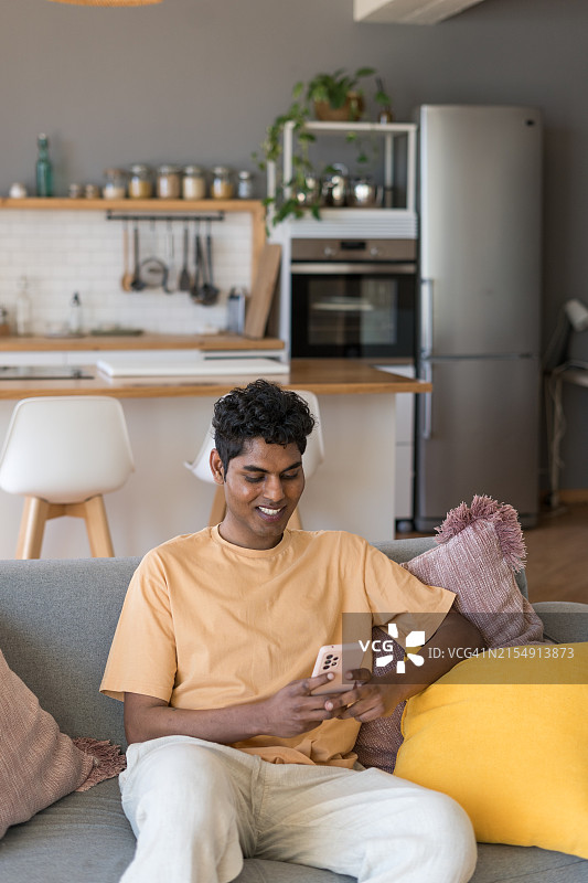 快乐的男人在家坐在沙发上使用智能手机图片素材