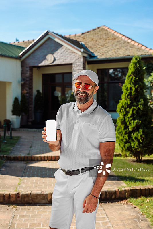 高尔夫球运动员站在房子外面，展示空白的手机屏幕图片素材