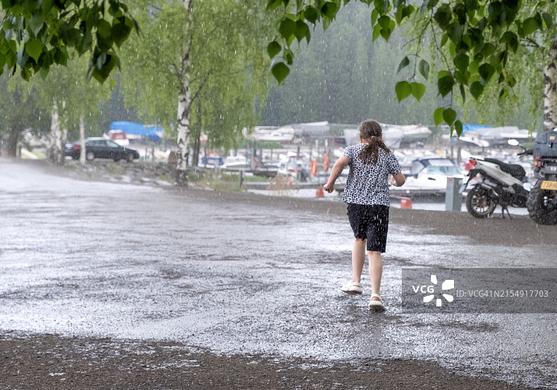 一个8岁的白人女孩在倾盆大雨中奔跑，从后方观看图片素材