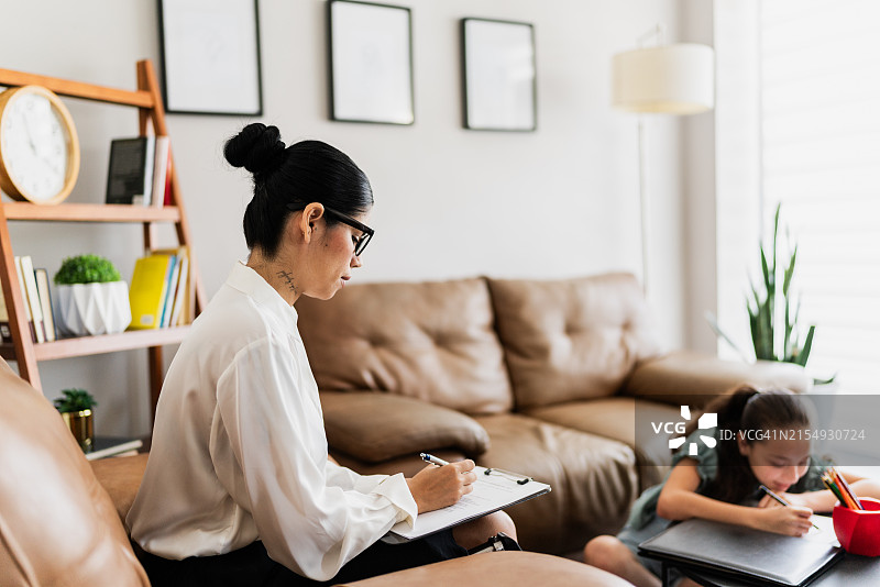 诊所治疗期间，中年女治疗师在剪贴板上书写，女童在绘画图片素材