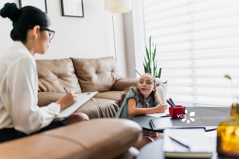 在诊所治疗期间，女童与中年治疗师交谈绘画图片素材