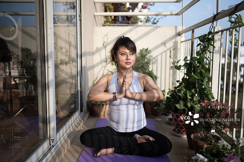 在阳台上练习瑜伽的宁静女人，可欣赏城市景观图片素材