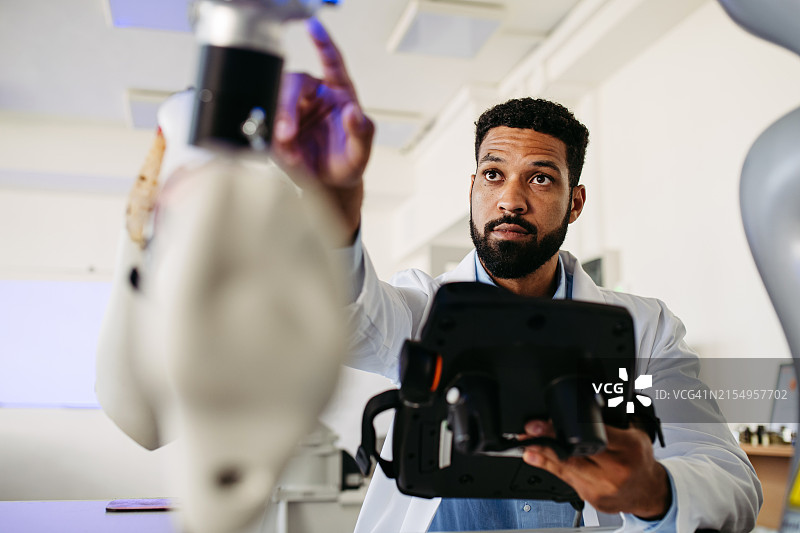 机器人工程师正在研究机器人膝关节置换手术项目，手持平板电脑，仔细观察。医疗保健中机器人技术、工程和计算机科学的概念。图片素材
