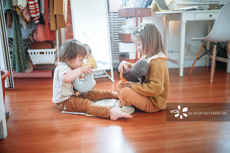 在室内地板上玩娃娃的兄弟姐妹图片素材