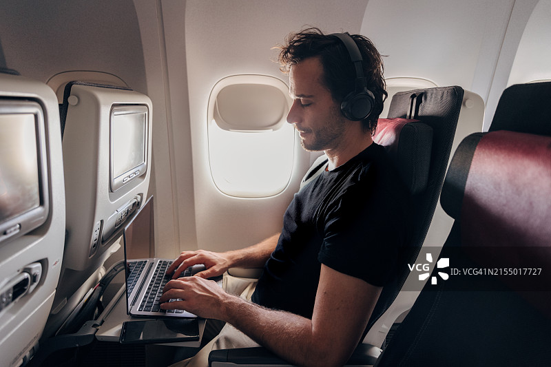 成年男人在飞行途中使用笔记本电脑和耳机图片素材