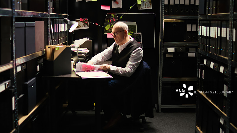 资深侦探在黑暗的房间里研究案件档案图片素材