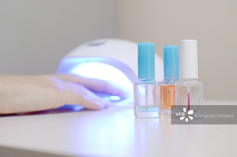 女性凝胶紫外线LED美甲背景下的三个无色透明指甲油瓶图片素材