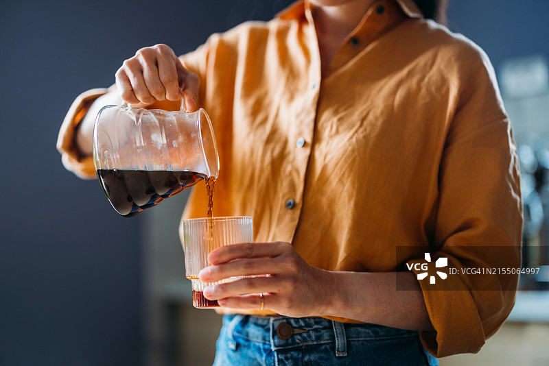 女人将新鲜冲泡的咖啡倒入玻璃杯中图片素材