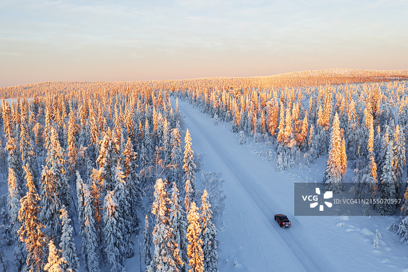 无人机视角：日出时分，汽车行驶在瑞典拉普兰松树林间的冰路上图片素材
