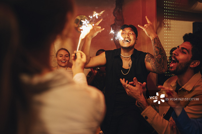 在夜总会里嘴里叼着燃烧的烟火棒并做出摇滚手势的无忧无虑的男人图片素材