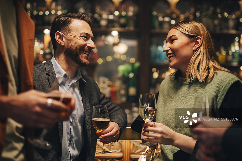 在酒吧拿着酒杯交谈的快乐男女朋友图片素材