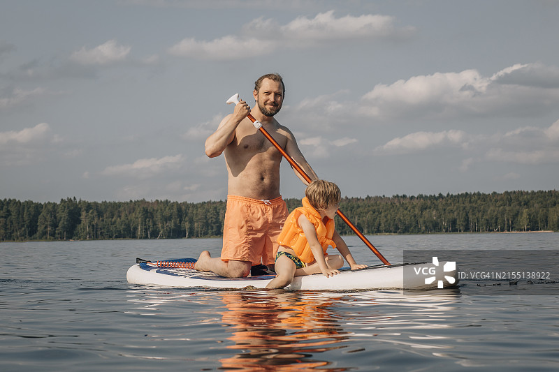 赤膊男人在晴天与儿子在海上玩桨板图片素材