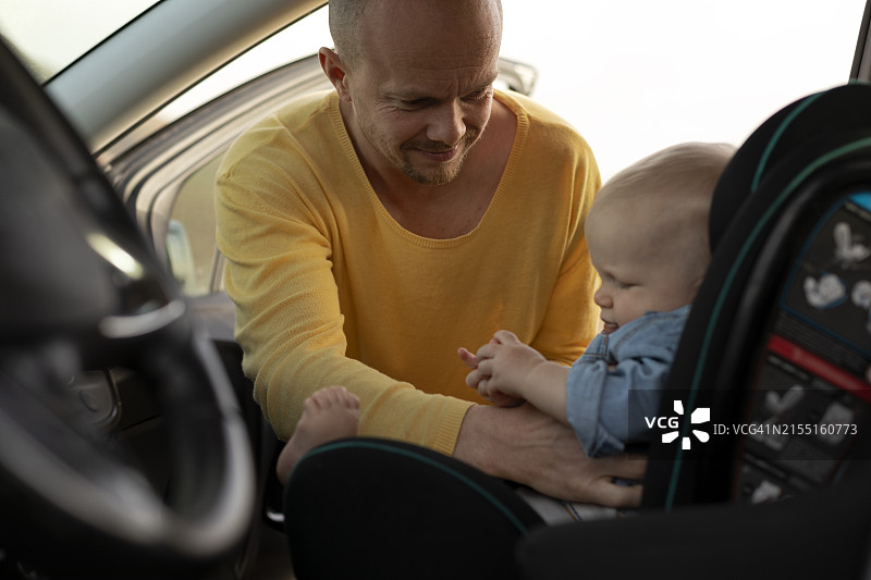 父亲为坐在车里的儿子系安全带图片素材