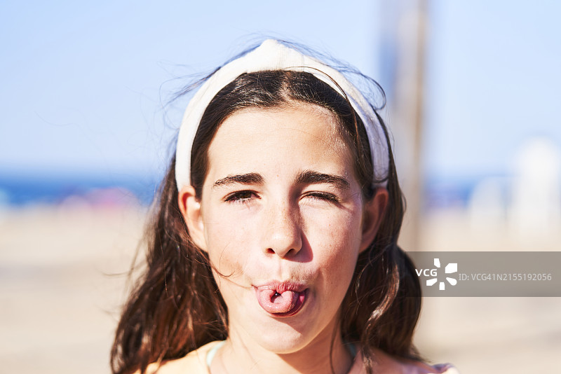 年轻女子在海滩上面对镜头做鬼脸吐舌微笑（正面视角）图片素材