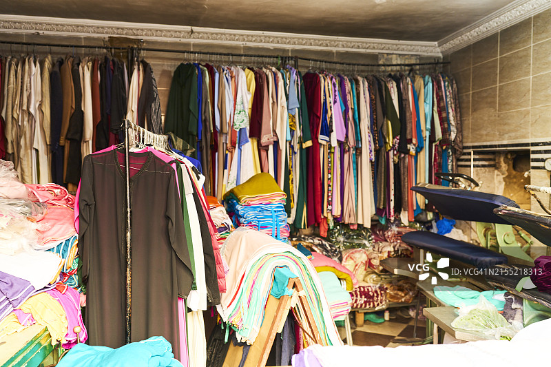 一家摆满凌乱衣服的商店，一些衣服挂在带有工业熨斗的大型衣架上图片素材