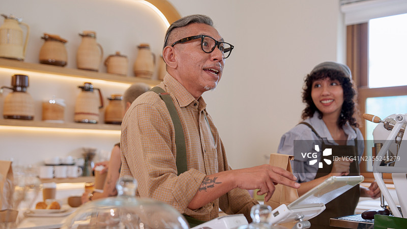 咖啡馆：服务员和年长男子在平板电脑上查看餐厅销售额图片素材