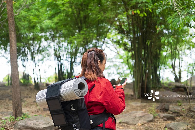 背包客在森林中使用带便携式太阳能板的智能手机图片素材