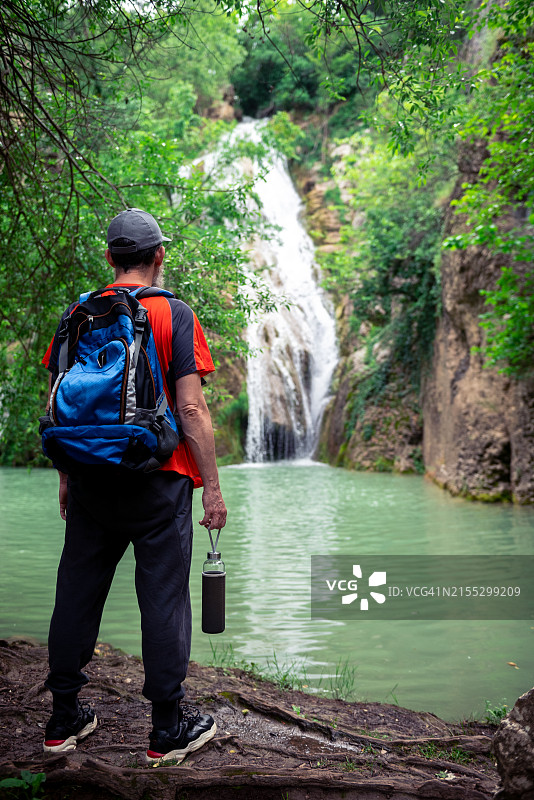 年长的男人在丛林中徒步，前方有瀑布图片素材