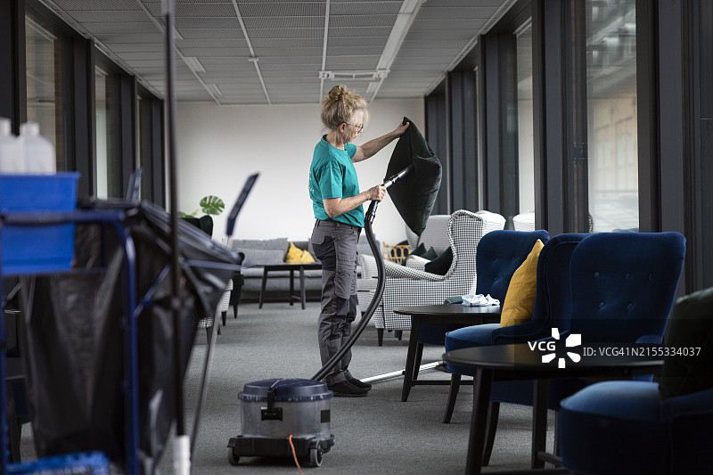 中年妇女清洁工用吸尘器清洁大堂坐垫图片素材