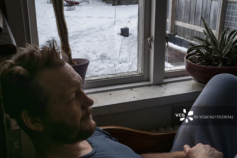 若有所思的男人坐在家里的客厅的窗边图片素材