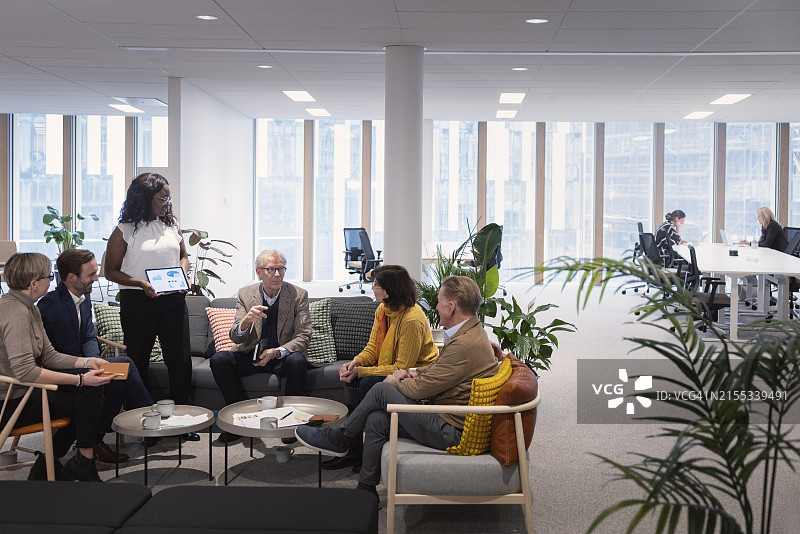 在办公室会议中与同事讨论平板电脑的女商人图片素材