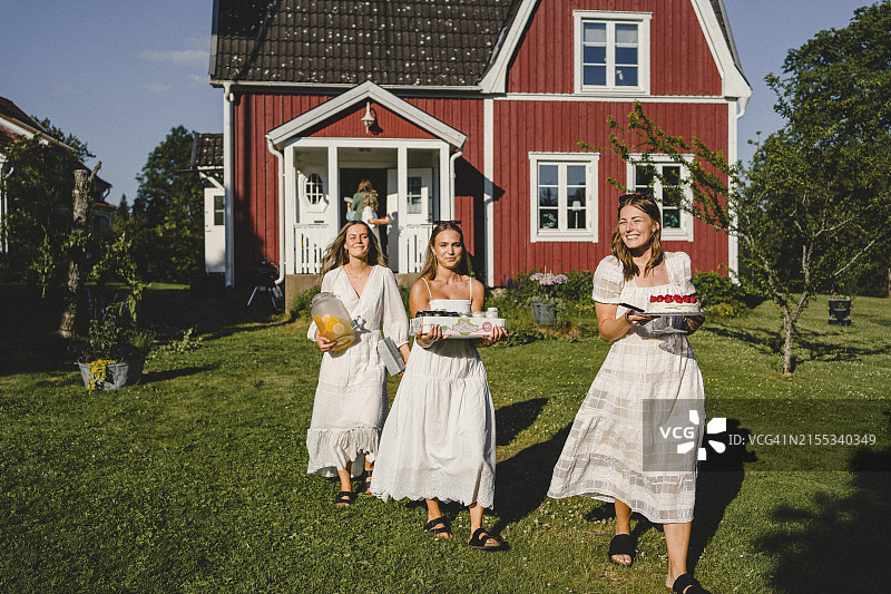 阳光明媚的日子里，年轻女性朋友在后院携带食物和饮料的全身像图片素材