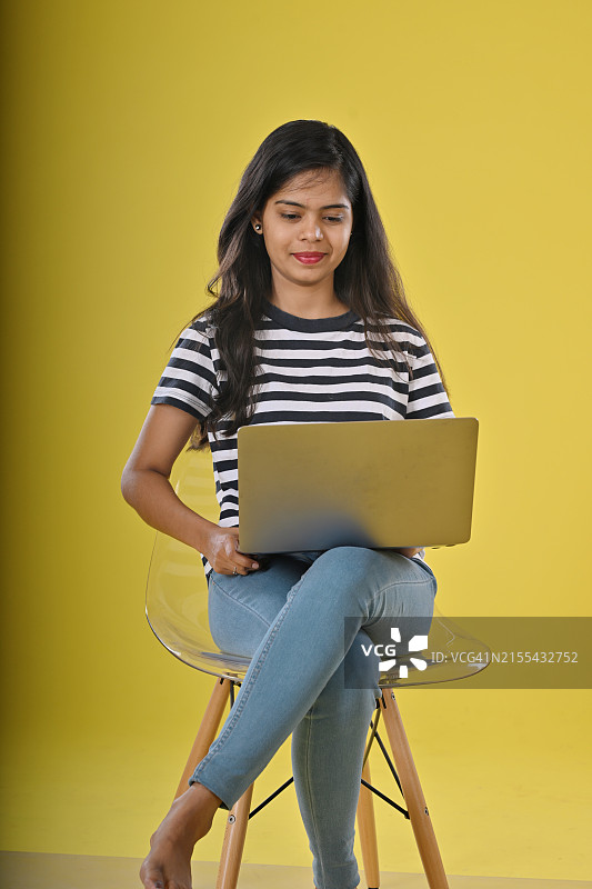 在彩色背景下用笔记本电脑工作的微笑年轻女子图片素材