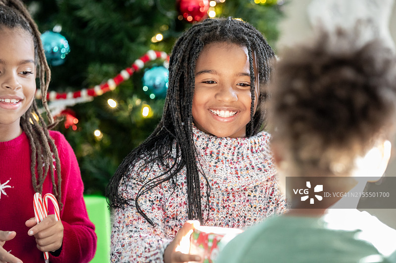 小学时期的兄弟姐妹在圣诞树的闪烁灯光下交换礼物，庆祝节日图片素材