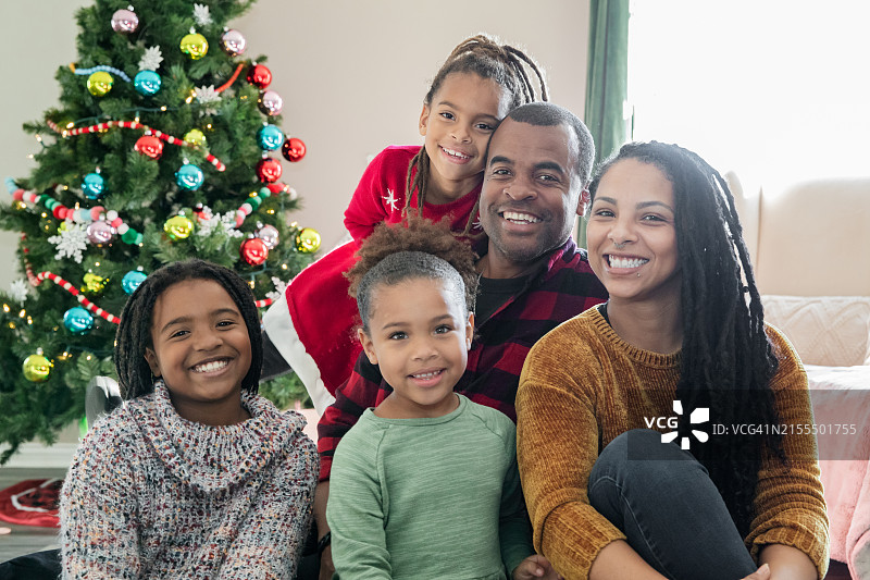 一家五口在明亮的圣诞树前交换圣诞礼物，拥抱节日的魔力图片素材