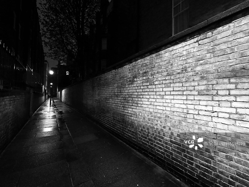 英国伦敦一条狭窄黑暗小巷的夜间风化砖墙。自然光。黑白的。无人。图片素材