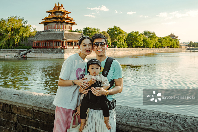 亚洲父母和男婴在日落时分靠近宁静的宫殿和水边图片素材