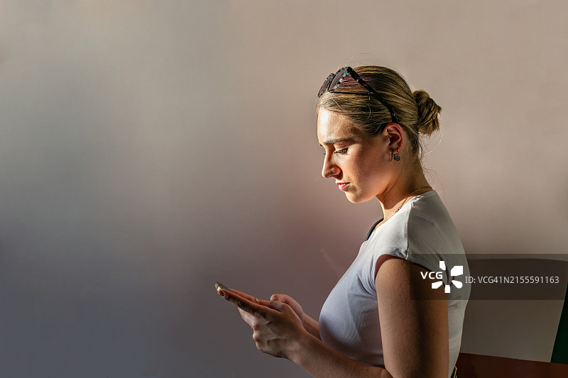 在商业区自然侧光照射下，看着手机的严肃而有魅力的年轻金发女子侧面照图片素材