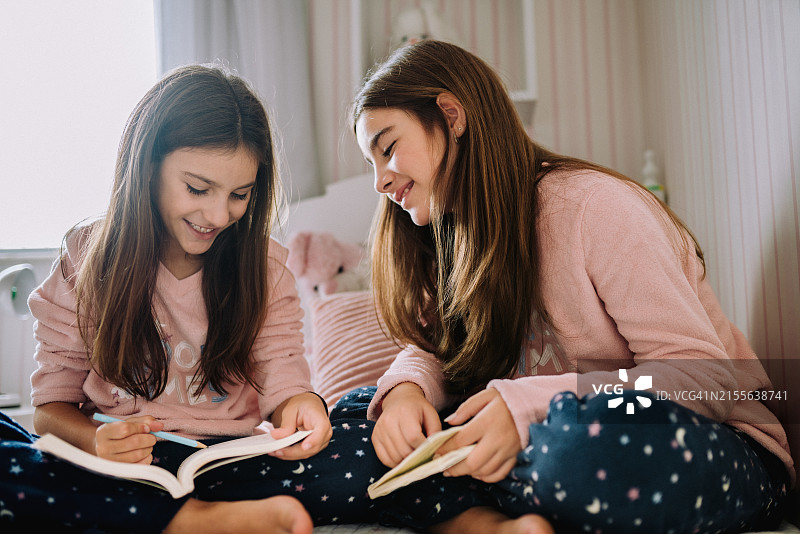 两个姐妹穿着睡衣坐在床上一起读书图片素材