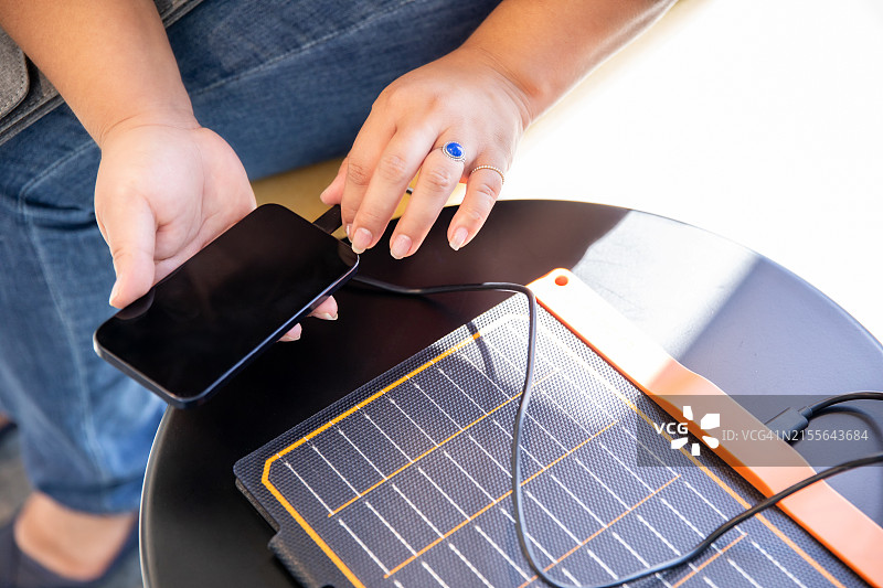 女人用便携式太阳能电池板为智能手机充电图片素材