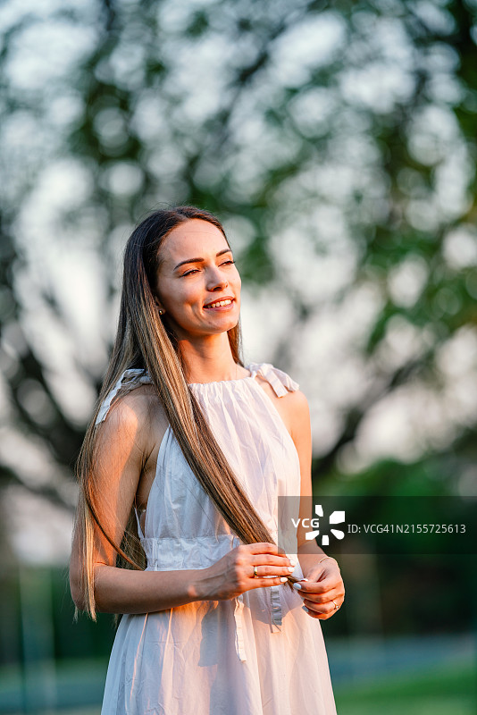 在日落时穿着白色连衣裙的美丽年轻女人肖像图片素材