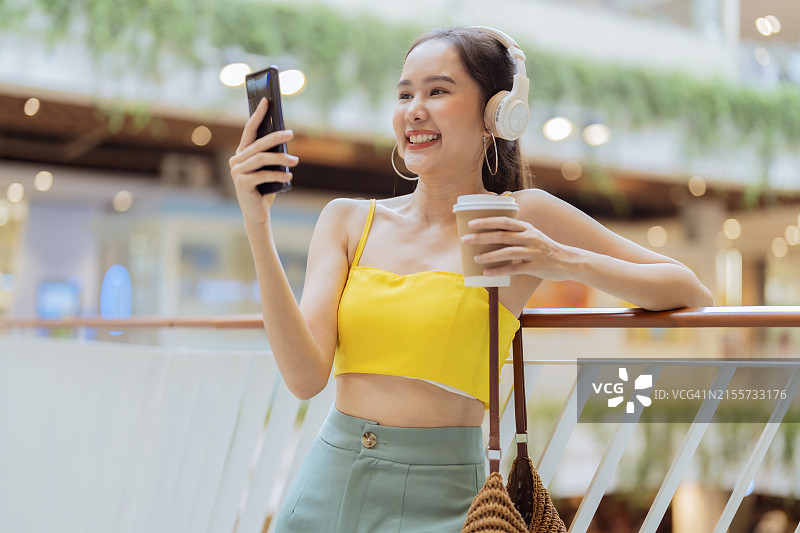 快乐的亚洲女性在购物中心听音乐，享受生活图片素材