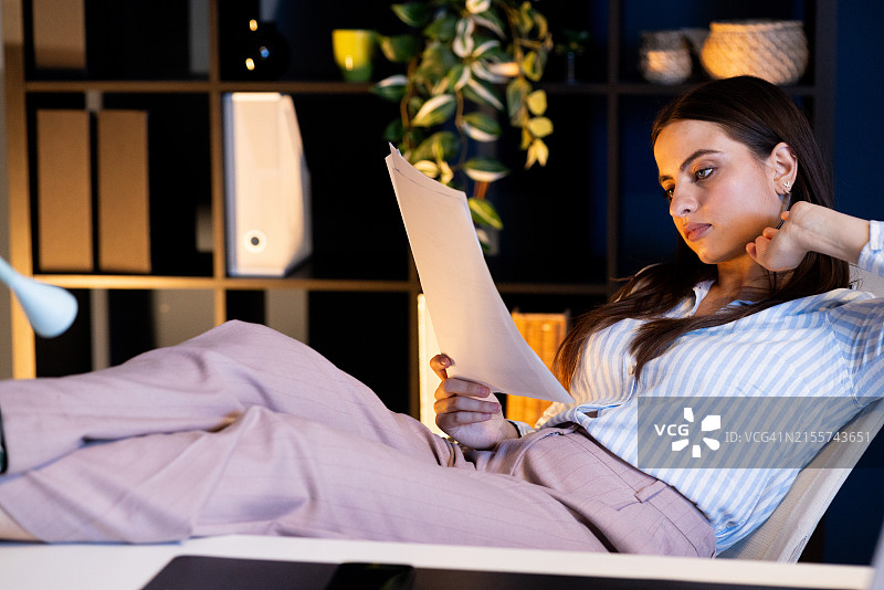 工作到很晚并在阅读一些商业计划的年轻女人图片素材