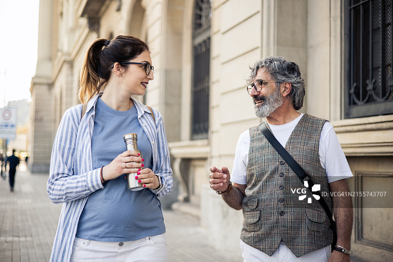年长的男人和怀孕的年轻朋友边走边聊图片素材
