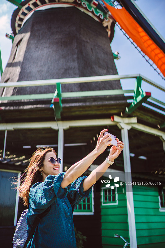 年轻亚裔女性在风车旁使用AI导游APP图片素材