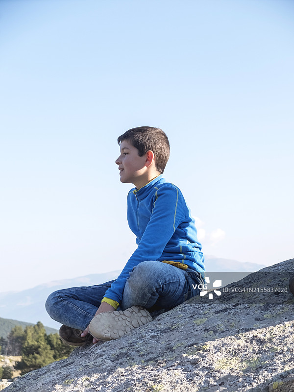 快乐的青少年坐在岩石上眺望远山图片素材